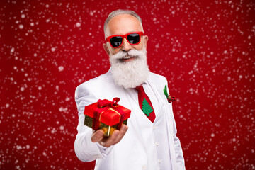 Poster - Photo of funky elder grey hair santa man give present wear eyewear white jacket isolated on red color background