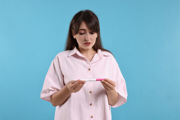 Poster - Worried young woman with pregnancy test on light blue background