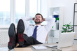 © New Africa - Smiling businessman with hands behind his head holding legs on table in office. Break time