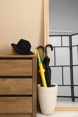 Wall Mural - Colorful umbrellas in holder, hat on wooden chest of drawers and mirror indoors