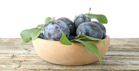 Wall Mural - Fresh plums and green leaves in bowl on wooden table against white background