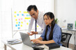 © Kritdanai - Focused Collaboration: A male and female Asian professional intently collaborate at a laptop, surrounded by brainstorming notes, embodying teamwork and problem-solving in a modern office.