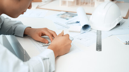 Wall Mural - Professional architect engineer drawing blueprint and working together with young beautiful caucasian coworker on meeting table with safety helmet, house model, blueprint scatter around. Immaculate.