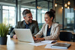 © Pixel Focus AI - Two busy happy professional business man and woman executive leaders team using laptop working on computer at work desk having conversation on financial project at meeting in office