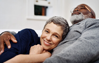 Wall Mural - Relax, smile and senior couple hug for love, care and support in living room at home. Interracial, man and woman embrace for connection in relationship, commitment and loyalty to partner in marriage