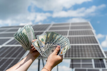 Wall Mural - Engineer holding dollar bills against solar energy panels, renewable energy