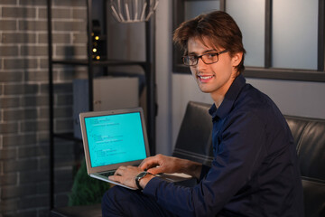 Wall Mural - Happy young businessman sitting on sofa in office and working with laptop