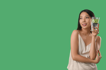 Sticker - Young Asian woman with glass of cucumber water on green background