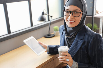 Wall Mural - Muslim businesswoman with tablet computer and cup of coffee at table in office