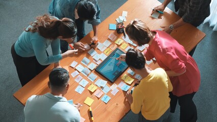 Top view of manager writing idea on sticky notes and explain idea about web design. Professional marketing team or programmer brainstorming idea while looking at tablet with color palette. Symposium.