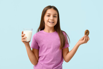 Happy little girl holding sweet chocolate cookie and glass of fresh milk on blue background