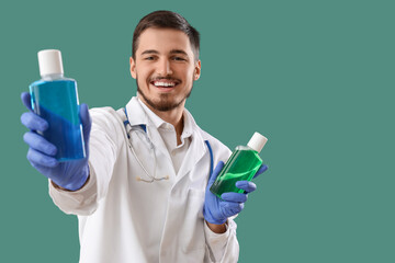 Wall Mural - Young male dentist with bottles of mouthwash on green background. Dental care concept