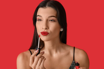 Sticker - Beautiful young woman applying bright lipstick on red background