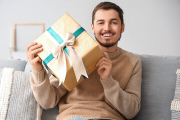 Canvas Print - Young man with gift sitting on sofa at home