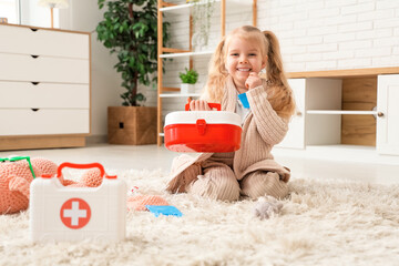 Wall Mural - Cute little girl with first aid kit playing doctor at home