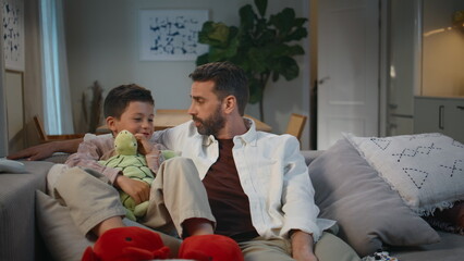 Wall Mural - Father son talking evening sitting sofa at living room. Cute toddler holding toy