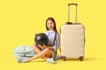 Wall Mural - Cute little tourist with globe and bags sitting on yellow background