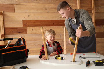 Wall Mural - Male worker with his little son assembling table in workshop