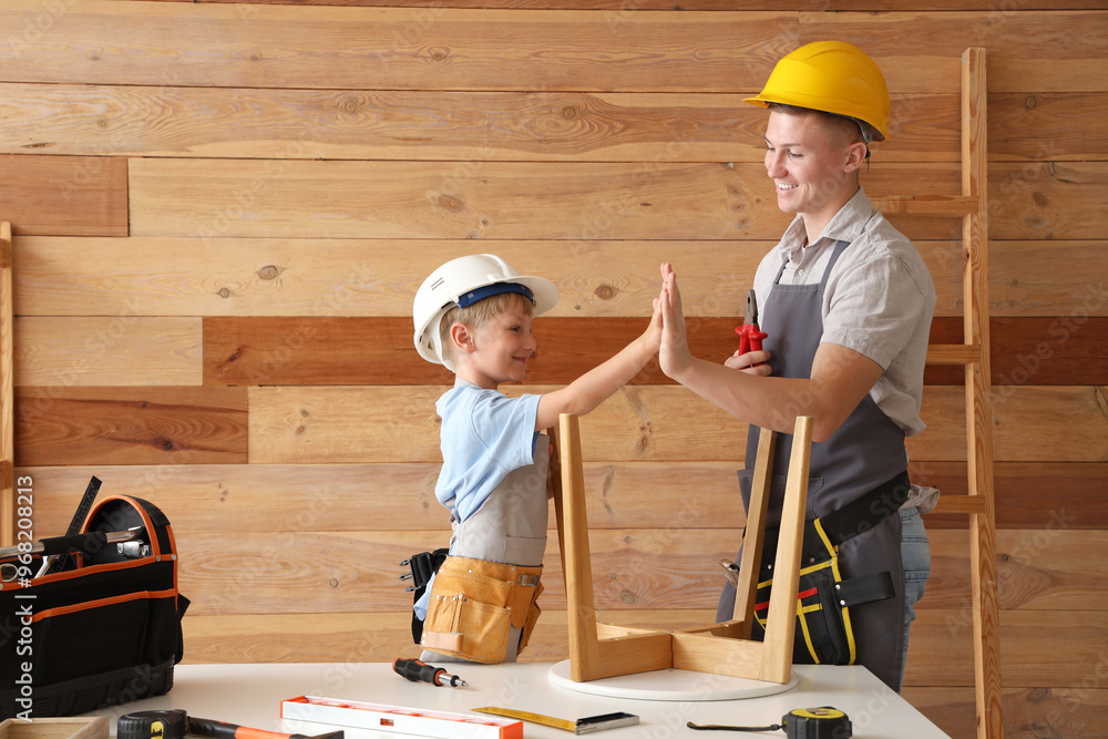 Male worker with his little son giving each other high-five in workshop