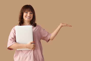 Wall Mural - Beautiful woman with laptop showing something on beige background