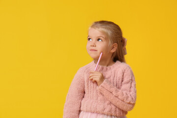 Wall Mural - Cute little happy girl in warm stylish sweater with pen on yellow background