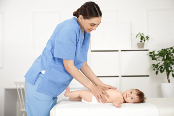 Wall Mural - Cute little baby getting belly massage from happy professional therapist on couch in clinic