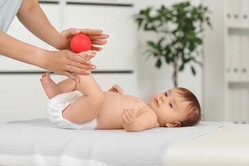 Sticker - Cute little baby getting foot massage with ball from professional therapist on couch in clinic