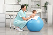 © Pixel-Shot - Cute little baby getting massage on fitball from happy professional therapist in clinic