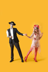 Wall Mural - Young happy couple dressed for Mexico's Day of the Dead (El Dia de Muertos) dancing on yellow background