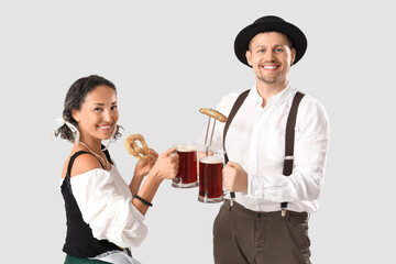 Happy mature waiters in traditional German clothes with mugs of beer, sausage and pretzel on grey background