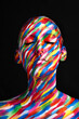 © SunriseDon/peopleimages.com - Color, art and face of woman with paint, creative identity and self expression with dark aesthetic in studio. Beauty, makeup and girl with cosmetic design, fantasy or rainbow skin on black background