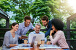 © BestCam/peopleimages.com - Collaboration, planning and technology with business people at restaurant for meeting outdoor. Documents, laptop and tablet with man and woman employee team at wooden table for brainstorming together