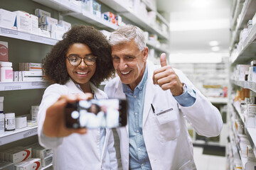 Canvas Print - Selfie, people and healthcare in pharmacy, smile and wellness of medicine, store and photography. Thumbs up, lab coat and pharmacist with mature man, shelf and confident with picture and memory