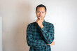 © Tito Rollis - Young Adult bearded Asian man wearing green flannel shirt showing thinking gesture. Hip on chin