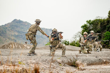 A group of military men in combat gear patrol in the middle of a desert and tropical jungle. Soldiers in full combat gear in dry weather conditions assemble and march on a mission.