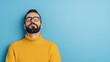 © ikkilostd - Young Middle-Eastern man in yellow sweater and glasses, relaxing against a blue background.