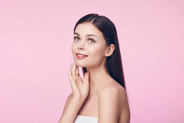 Wall Mural - Beautiful young woman with glowing skin posing with her hands on her face against a pink background