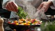 © siripimon2525 - A chefs hands tossing fresh herbs into a sizzling pan of vegetables, steam and vibrant colors adding energy to the shot