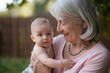 © D-point - Grandmother holding baby outdoors. Warm family moment. Generational bonding concept. Perfect for family care, parenting content. Photo for greeting cards, social media, advertising with copy space.