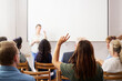 © Johnér - Businesswoman with hand raised sitting behind colleagues during meeting in office