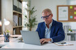 © Phimwilai - Senior male businessman in glasses uses laptop to check documents Analyze data in business operations in the office.