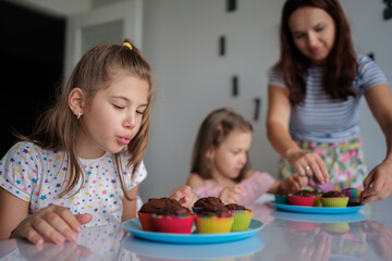 A joyful scene of a mother and two daughters baking chocolate cupcakes. The children are excited as they decorate the treats, enjoying quality family time in a cozy kitchen setting.