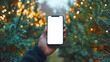 © chekart - A black man is holding a smartphone in his hand. A mockup of the phone on the background of fir branches decorated with glowing garlands. Advertising discounts, promotions and sales
