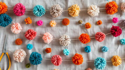 Wall Mural - A flat lay of a completed yarn pom-pom garland, with colorful pom-poms strung together and extra yarn, scissors, and needles neatly placed on a soft fabric background.