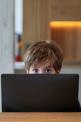 A young boy is sitting at a table with a laptop in front of him