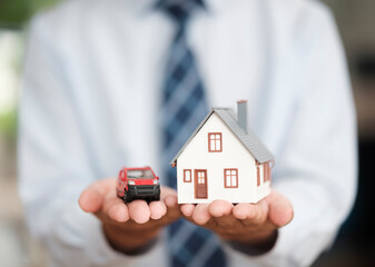 Wall Mural - Real Estate Agent Holding House and Car Models Symbolizing Property and Vehicle Insurance