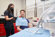 © Oscar - latina woman dentist putting a bib on a smiling man sitting in the chair to perform a procedure