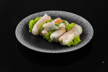 Plate of fresh spring rolls on a bed of lettuce, presented on a black background, minimalistic and elegant food photography.