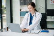 © Nuttapong punna - Young female doctor in white medical uniform using laptop and tablet talking video conference call at desk,Doctor sitting at desk