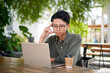 © fery - Young asian man thinking while looking to his laptop. Man working on his laptop at the outdoor cafe in the morning